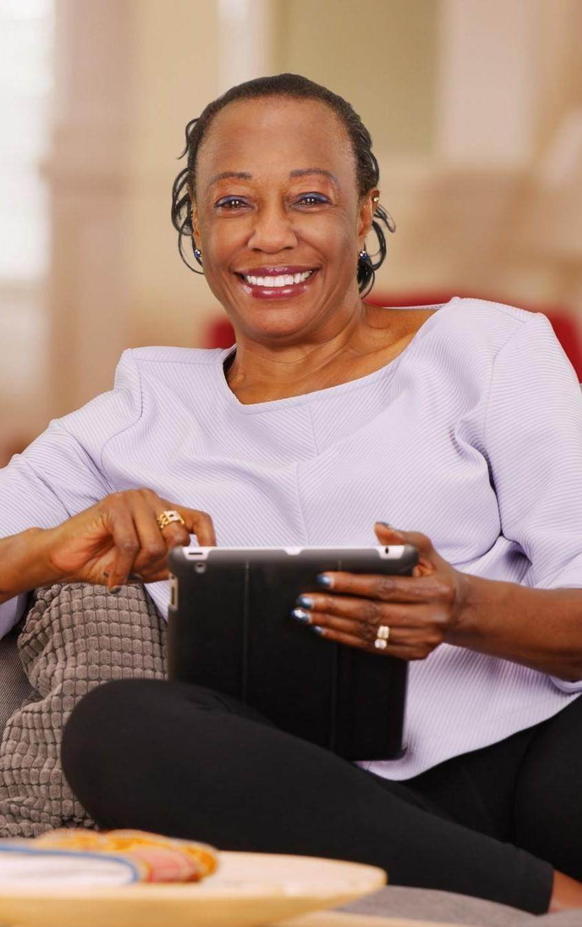 An elderly black woman happily uses her tablet while looking at the camera An elderly black woman happily uses her tablet while looking at the camera